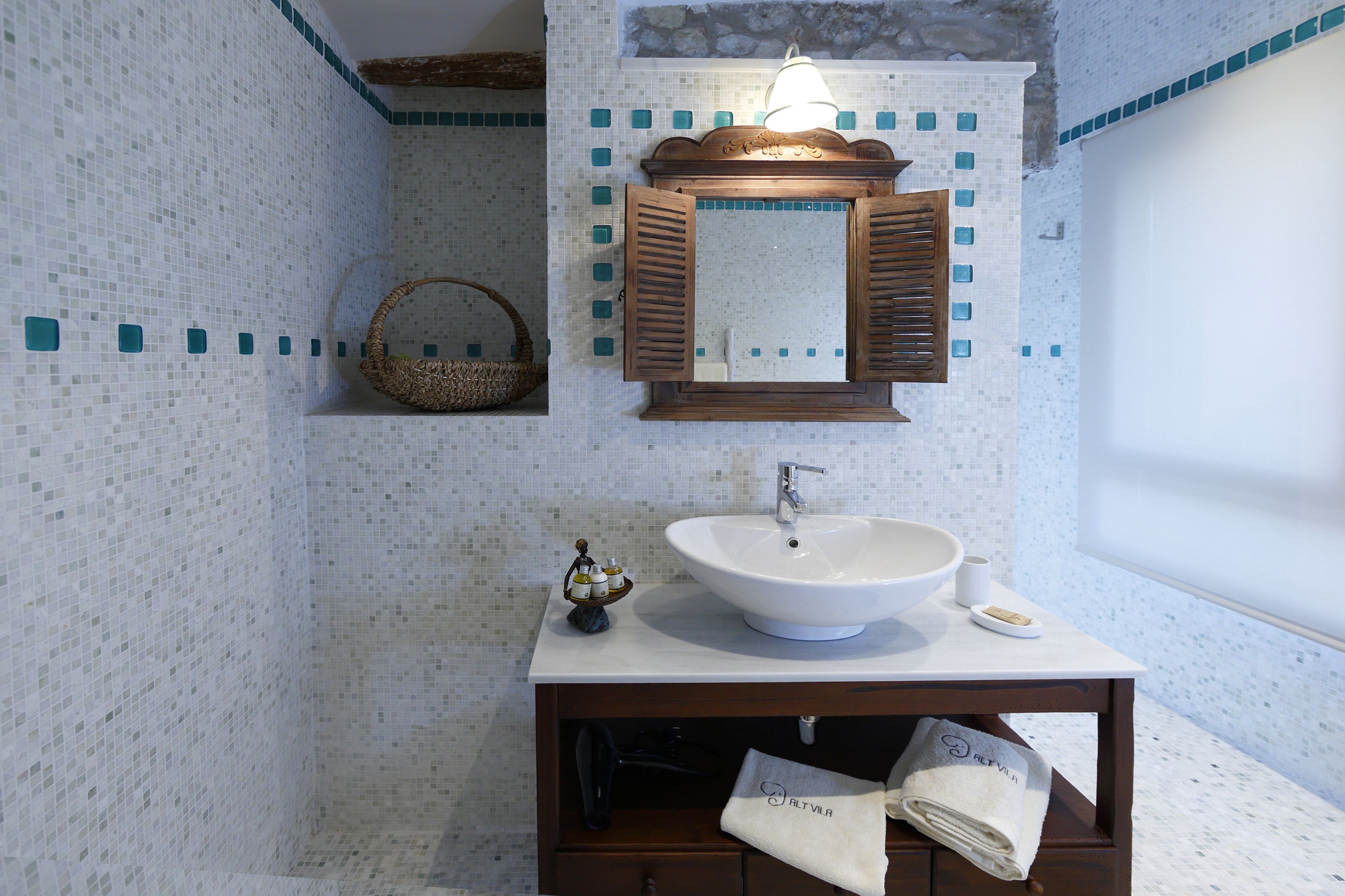 A bathroom with a white sink, wooden vanity, and a mirror with shutters.