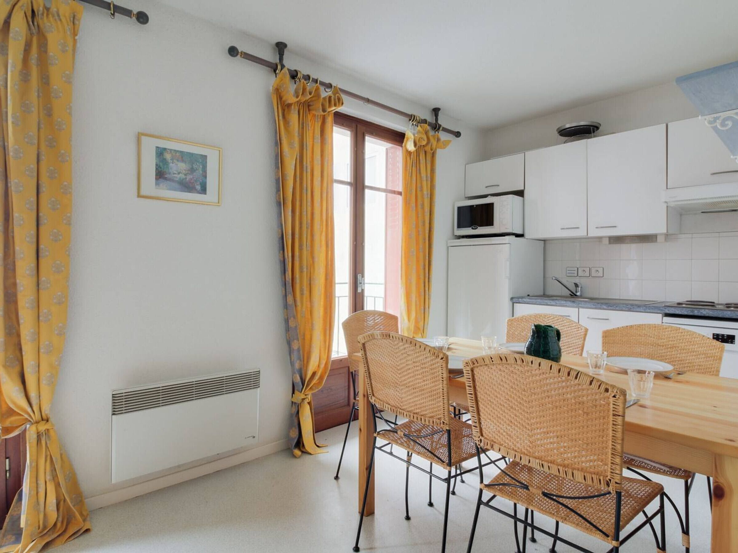Un coin repas avec une table en bois et des chaises en osier, un réfrigérateur blanc et un four à micro-ondes dans la cuisine.