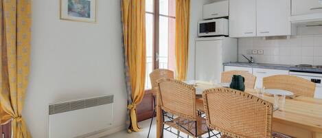 Un coin repas avec une table en bois et des chaises en osier, un réfrigérateur blanc et un four à micro-ondes dans la cuisine.