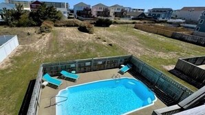 Un patio trasero con piscina, sillas de descanso y una terraza de madera.