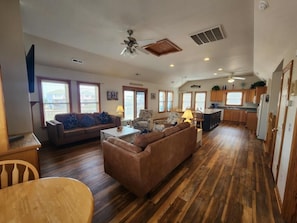 A spacious living room with a large brown sofa, a dining table, and a kitchen area with wooden cabinets and a countertop. - Free Private Heated Pool, Hot Tub, Fall flex stays, Pets OK, Rec. Room, Close to Beach & Restaura... (Kill Devil Hills)