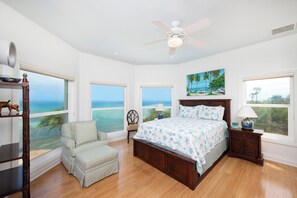 A bedroom with a large bed, a chair, a nightstand, and a ceiling fan.