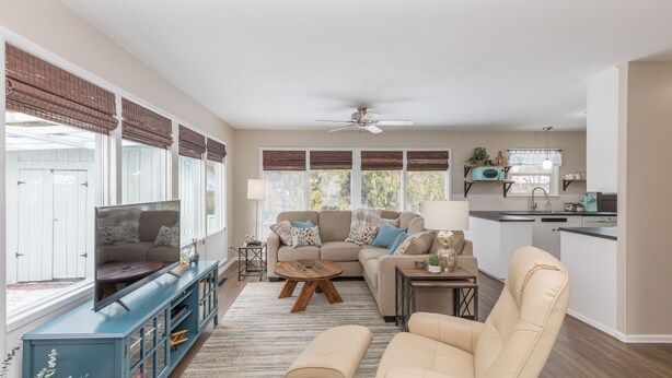 A spacious living room with a television, sofa, and coffee table. There is a kitchen area with a sink and cabinets.