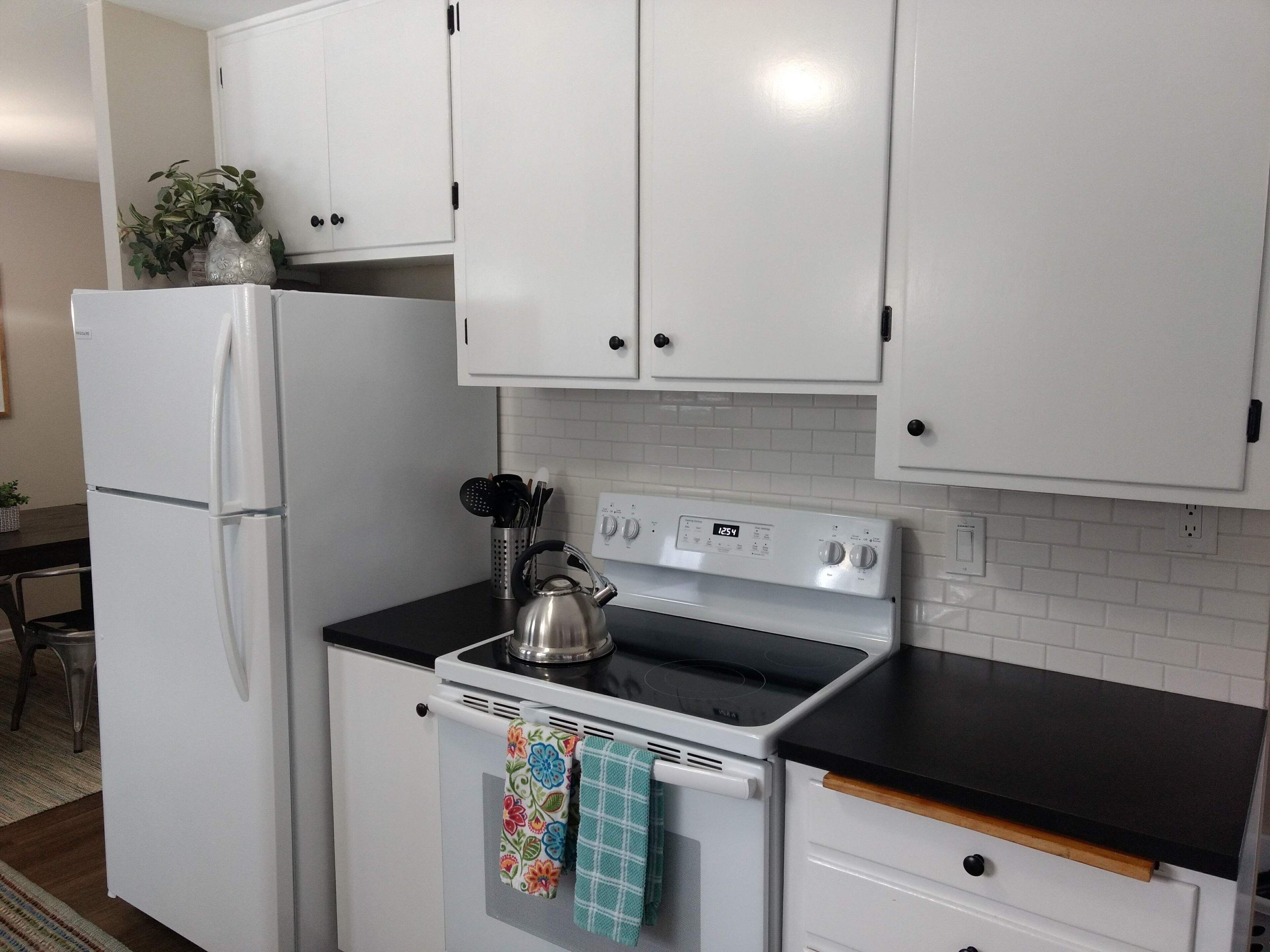 A kitchen with white cabinets, a white refrigerator, a stove, and a kettle.
