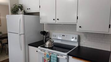 A kitchen with white cabinets, a white refrigerator, a stove, and a kettle.