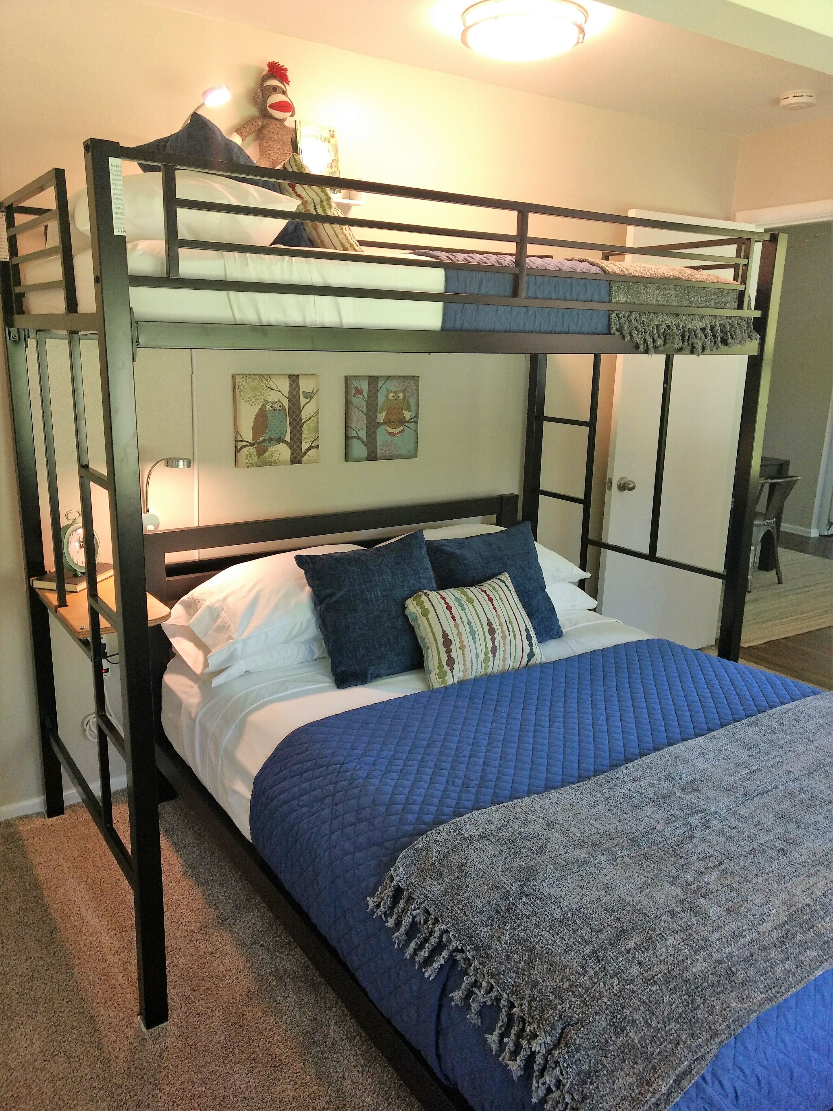 A bunk bed room with a blue quilted bedspread, pillows, and a blanket. There are wall art pieces and a lamp on the bunk bed.
