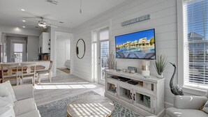 A modern living room with a large TV, a dining area, and a kitchen in the background.