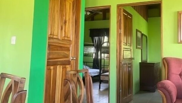 Ein Zimmer mit Holzwänden und einer grünen Tür, ein Holzstuhl, ein kleiner Tisch und ein roter Sessel.
