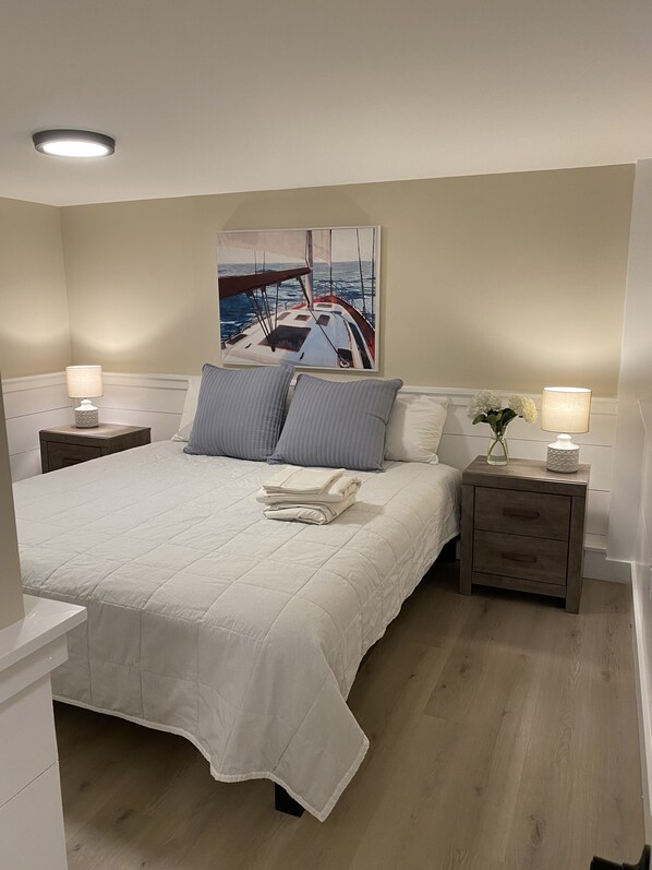 A bedroom with a large bed, two nightstands with lamps, a painting of a sailboat, and a vase with flowers. - Ocean View house for rent in stunning Falmouth Heights !!! (Falmouth)