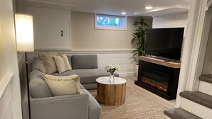 Un salon moderne avec un canapé gris, une table basse ronde en bois, une cheminée et un téléviseur.