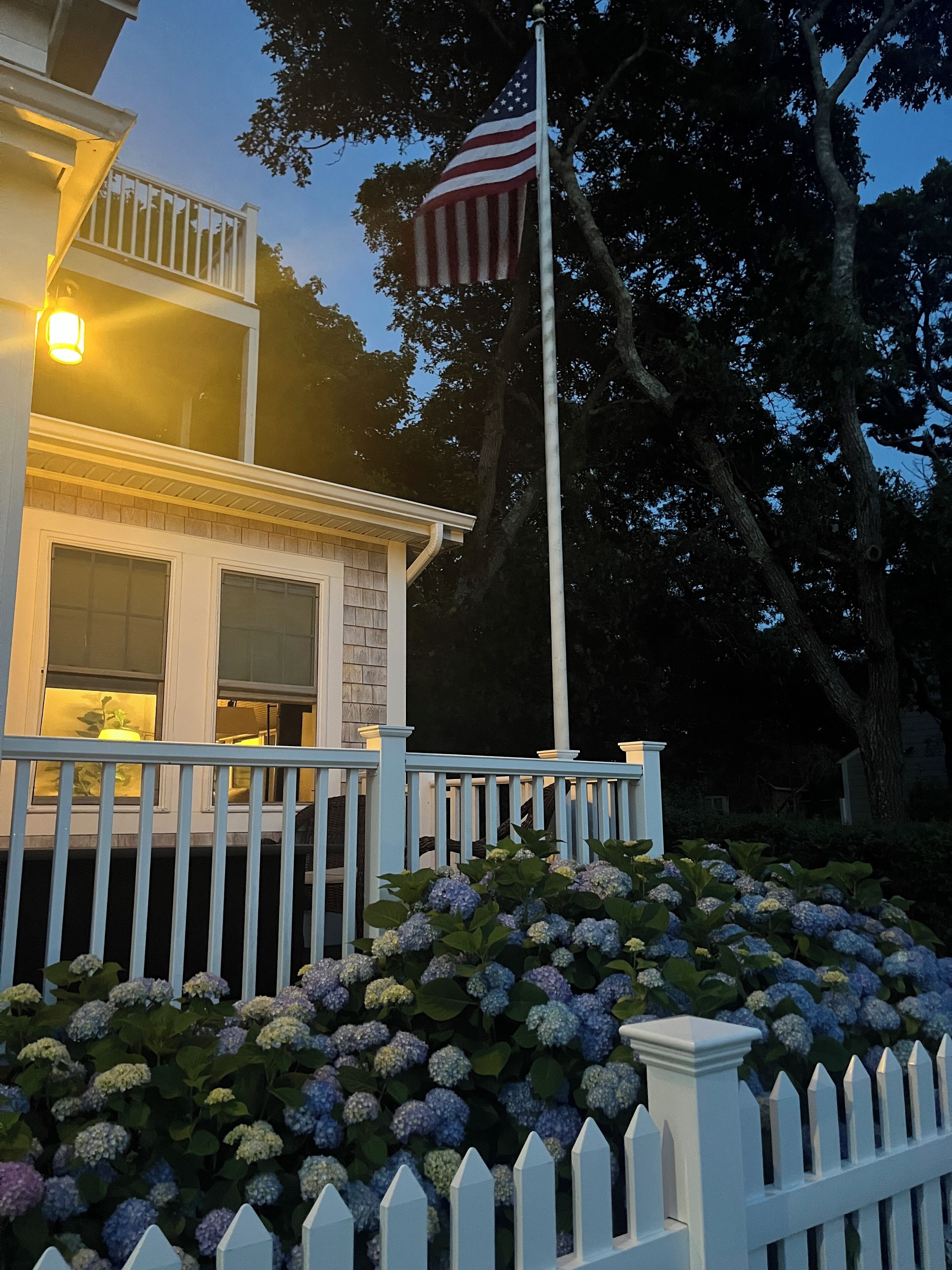 A house with a white picket fence, a balcony, and a flagpole with an American flag.
