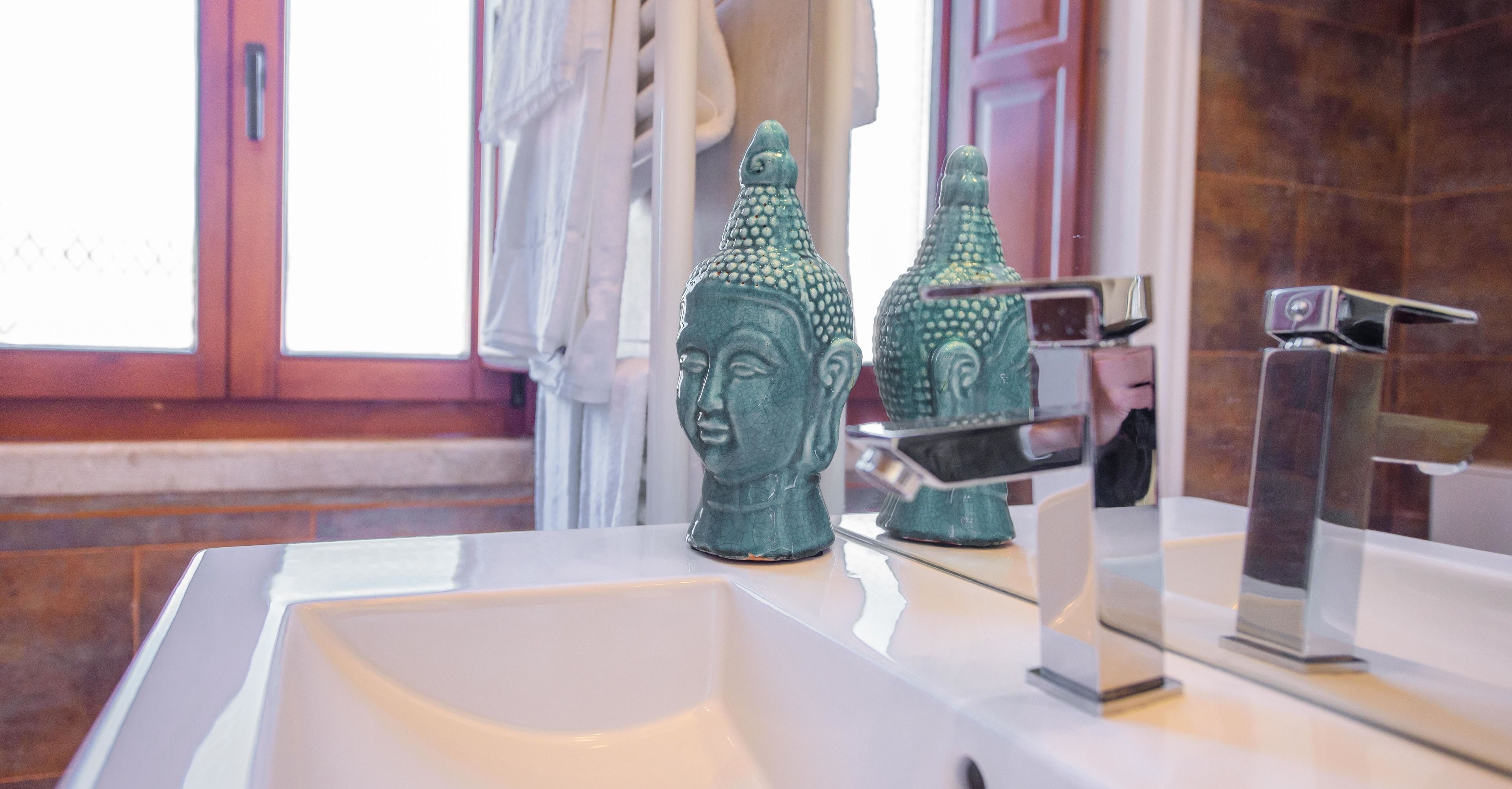 Un baño con un lavamanos blanco, dos jarrones verdes decorativos, un espejo y un grifo moderno.