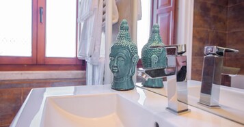 Un baño con un lavamanos blanco, dos jarrones verdes decorativos, un espejo y un grifo moderno.