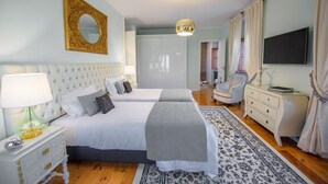 Ein Hotelzimmer mit zwei Betten, einem großen Spiegel, einer Chandelüster, einer weißen Kommode und einem Fernseher.
