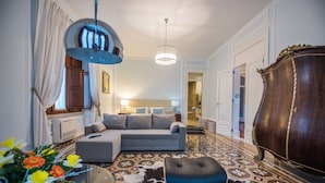 Ein modernes Wohnzimmer mit einem grauen Ecksofa, einem schwarzen Hocker, einem gemusterten Teppich, einer dunklen Holzkommode und einer Pendelleuchte.