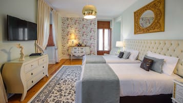 A hotel room with two beds, a dresser, a television, a mirror, and a floral wallpaper.