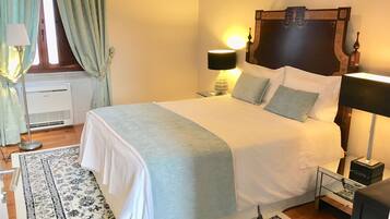 A neatly made bed with a white and light blue bedspread, two bedside lamps, a small bedside table with a lamp, a decorative headboard, and a patterned rug on the floor.