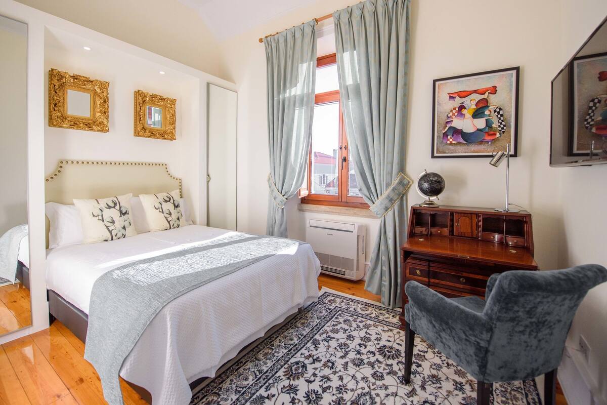 Une chambre à coucher avec un lit, un bureau, une chaise, un globe terrestre et des œuvres d’art accrochées aux murs.