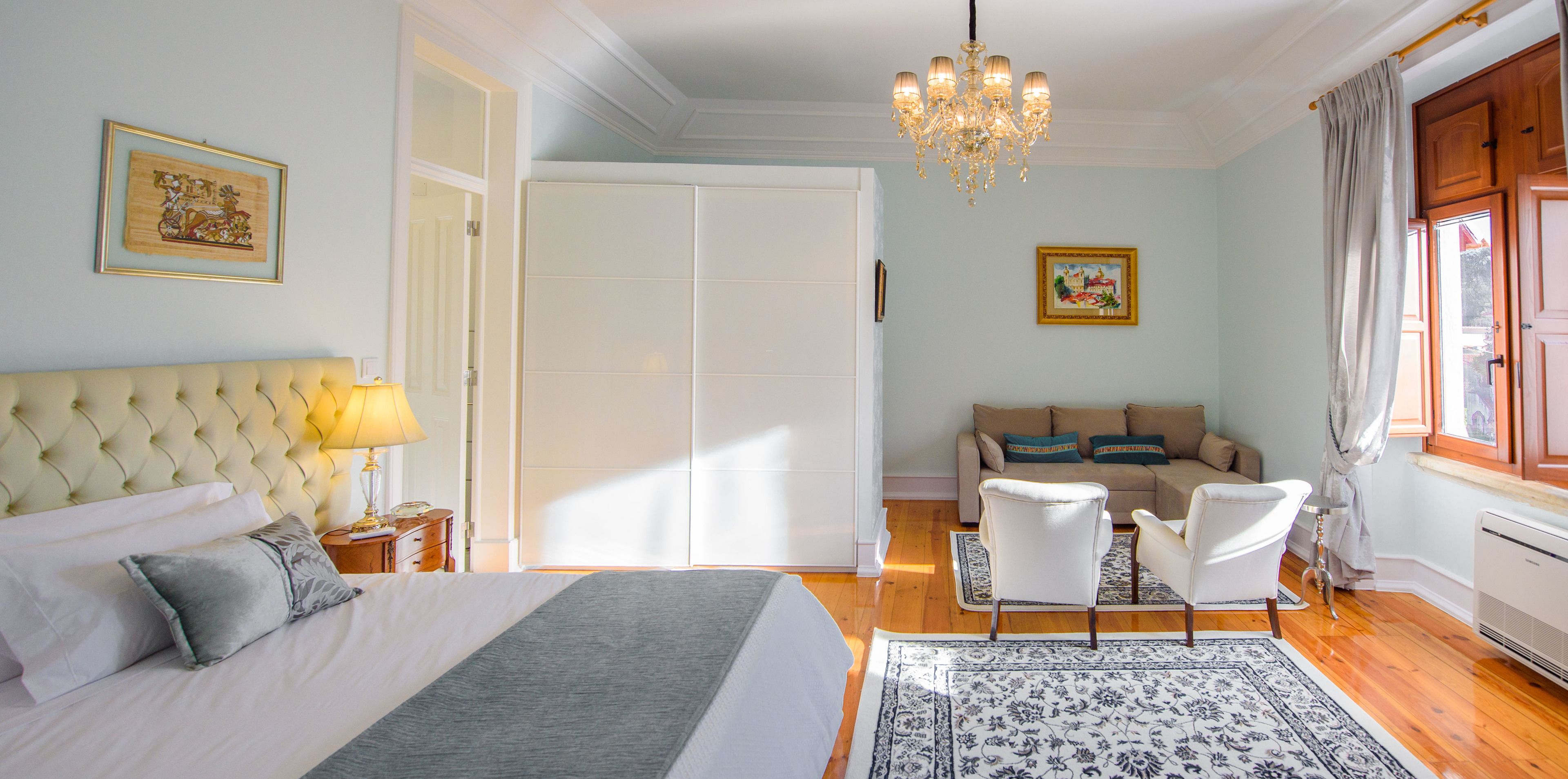 A bedroom with a large bed, a sofa, a chandelier, and a window with curtains.