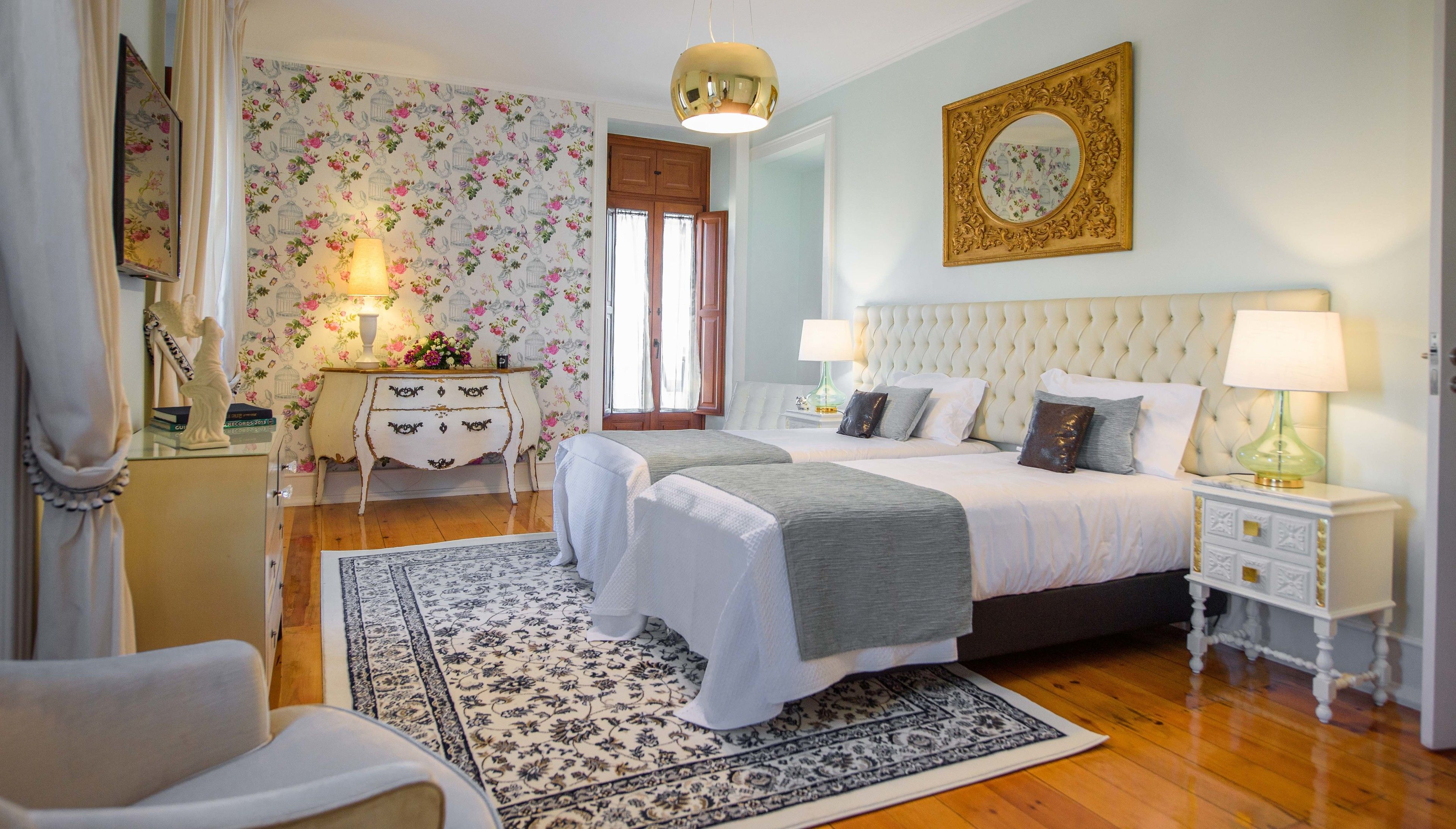 Quarto com uma cama grande, duas mesinhas de cabeceira, cômoda, espelho e tapete estampado.