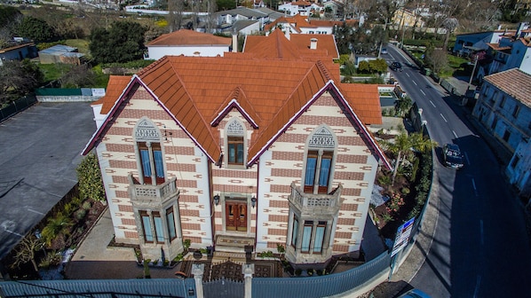 A two-story building with a red-tiled roof, a central entrance with a door, and two symmetrical windows with decorative frames. - Vila Vitorino (Sintra)