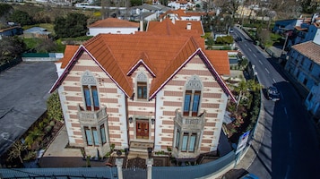 Un edificio de dos pisos con techo de tejas rojas, una entrada central con puerta y dos ventanas simétricas con marcos decorativos.