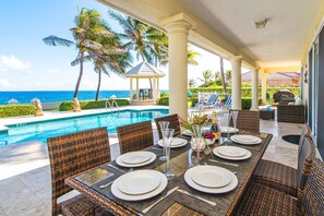 A poolside dining area with wicker furniture, a gazebo, and a view of the ocean.