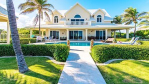 Una amplia casa de dos pisos con piscina, rodeada de césped cuidado y palmeras.