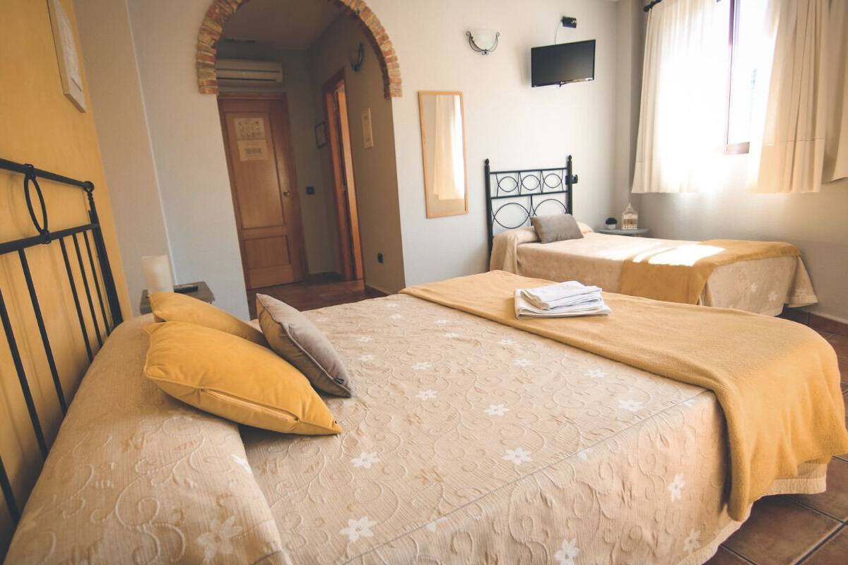 A hotel room with two beds, each with a headboard and a yellow pillow. There is a television mounted on the wall and a window with curtains.