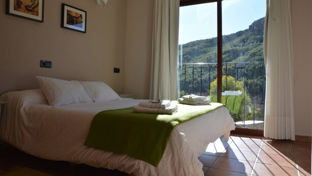 Un dormitorio con cama, balcón y vistas a un paisaje montañoso.