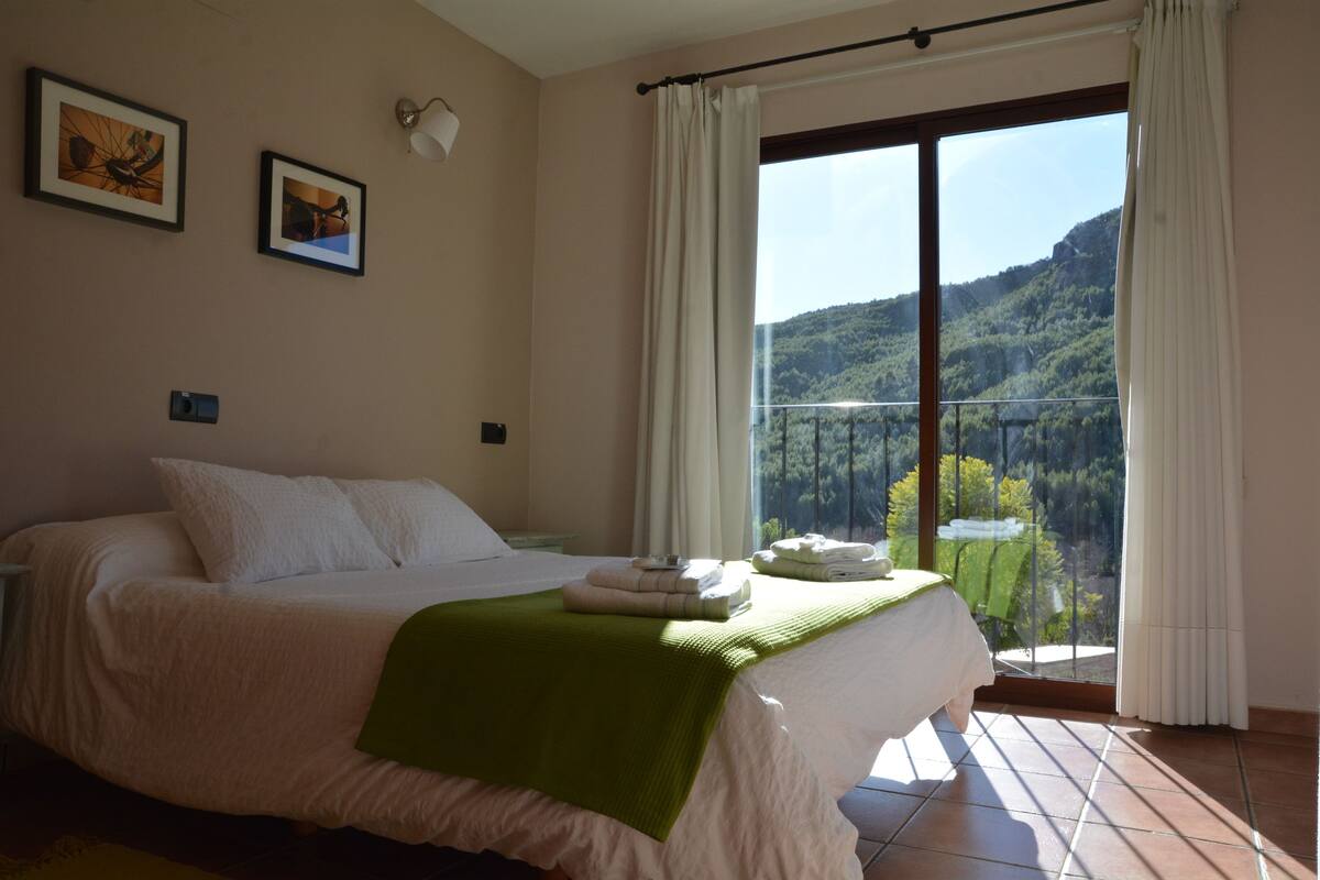 A bedroom with a bed, a balcony, and a view of a mountainous landscape.