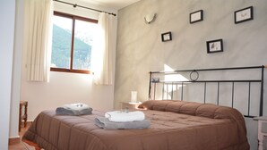 Un dormitorio con una cama grande, una ventana con cortinas, una mesita de noche con lámpara y cuadros enmarcados en la pared.