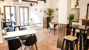 Un comedor con mesas y sillas de madera, una zona de bar con taburetes y plantas en macetas.