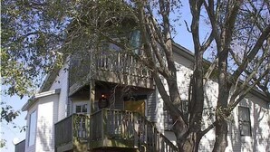 Un bâtiment à deux étages doté d’un balcon au deuxième étage, d’un grand arbre à l’avant et d’une clôture en piquets.