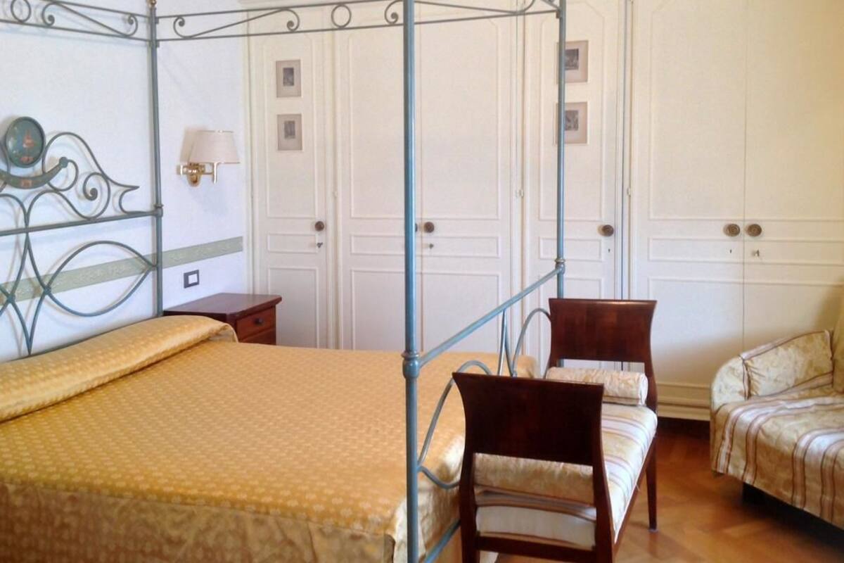 Un dormitorio con cama con dosel, una silla de madera, un sofá y un armario con espejo.