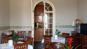 Un comedor con sillas y mesas de madera, una araña y un televisor sobre un mueble.