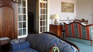 Una habitación con un sofá de color azul con estampado, un aparador de madera, una cama con cabecera floral y una araña.