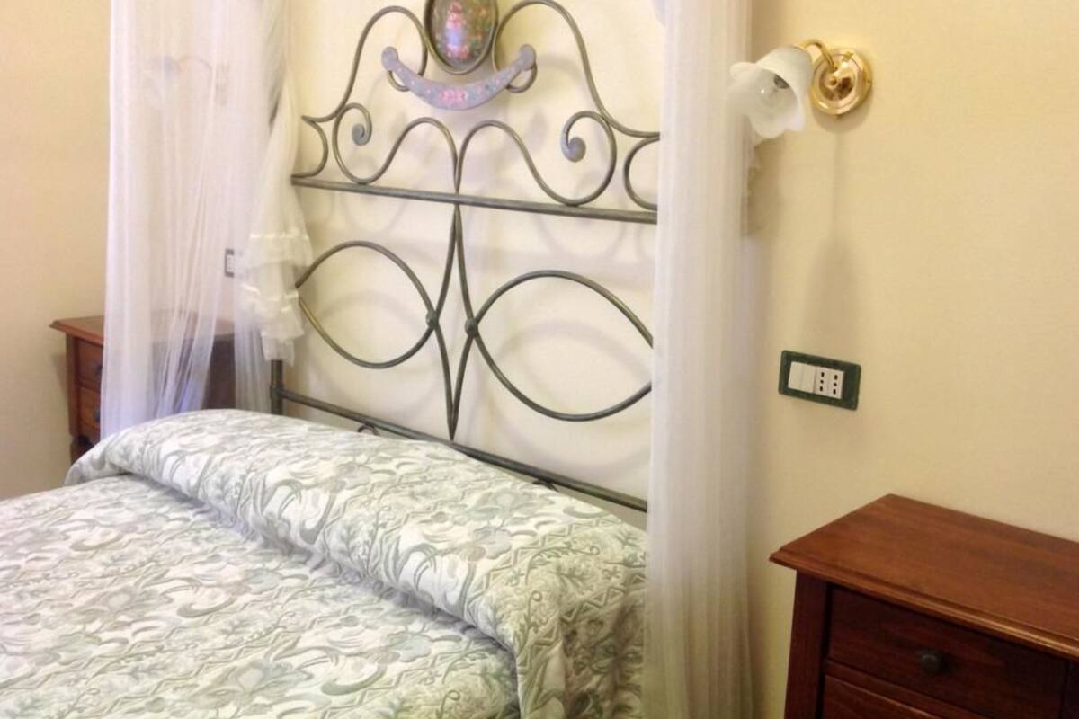 Una cama con cabecera de metal, una mesita de noche y un enchufe en la pared.