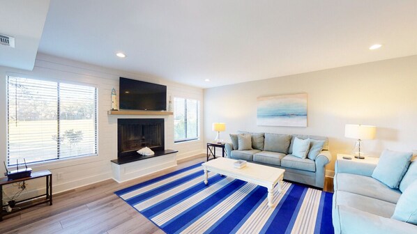 A living room with a fireplace, a sofa, a coffee table, and a TV mounted on the wall. - Recently Updated Beautiful Villa Directly on the Fazio Golf Course! (Hilton Head)