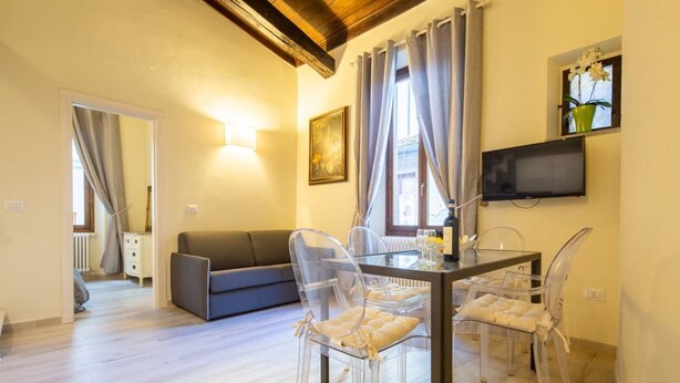 Un comedor con una mesa y sillas, un televisor montado en la pared y un ventanal con cortinas.