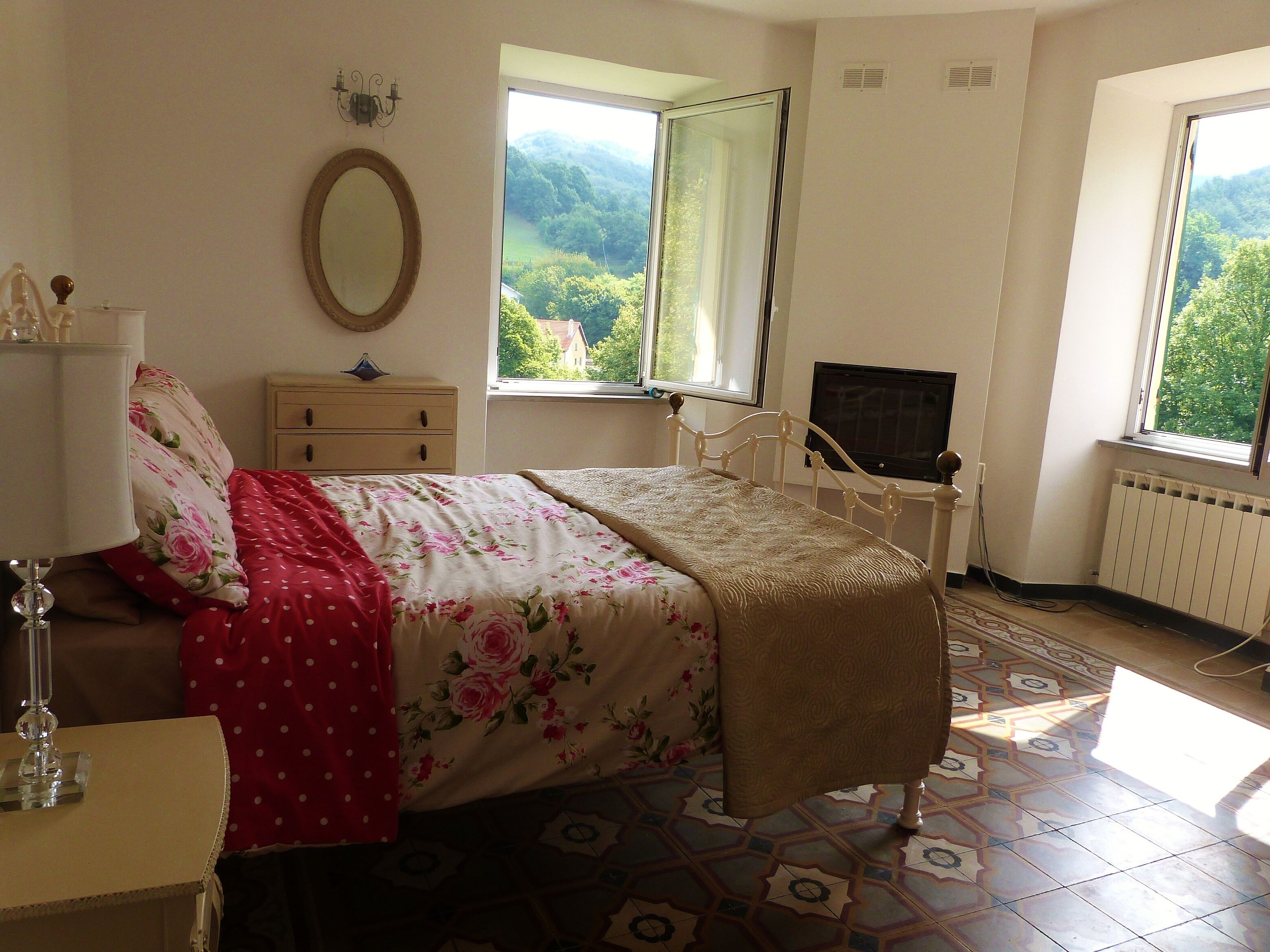 A bedroom with a bed, dresser, mirror, and a window with a view of greenery.