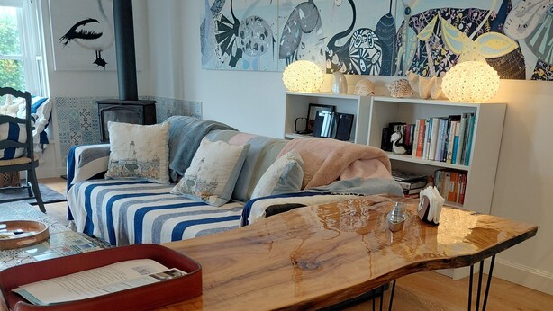 Una sala de estar acogedora con un sofá, una mesa de centro de madera, un banco, una estantería y adornos en la pared.