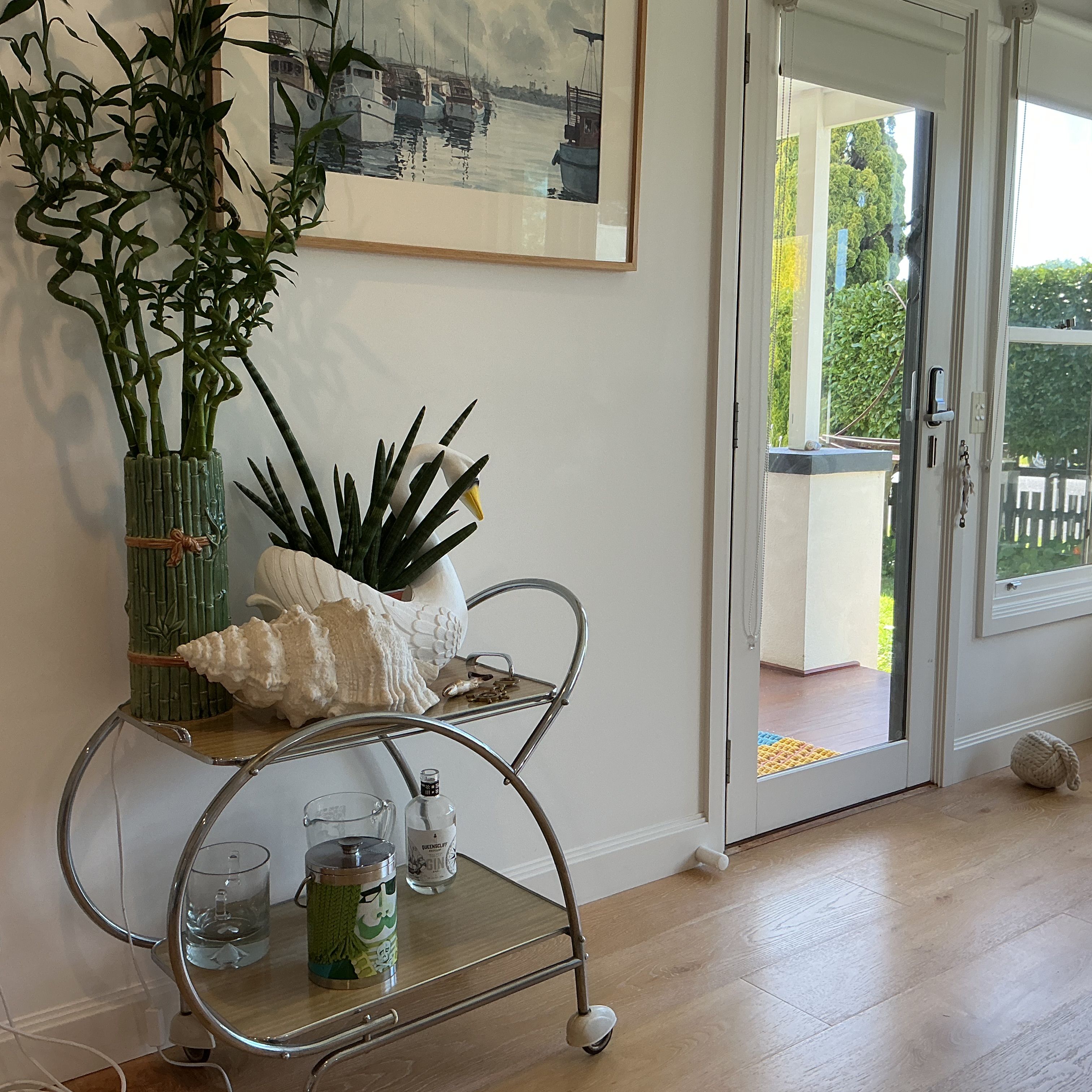 A room with a metal cart holding a plant, a framed artwork, and a glass container.
