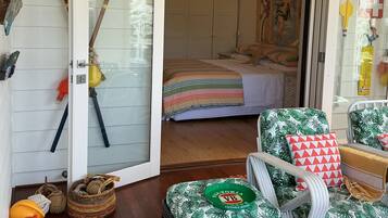 Quarto com uma cama, uma cadeira estampada com tema tropical, um cesto e uma mala.