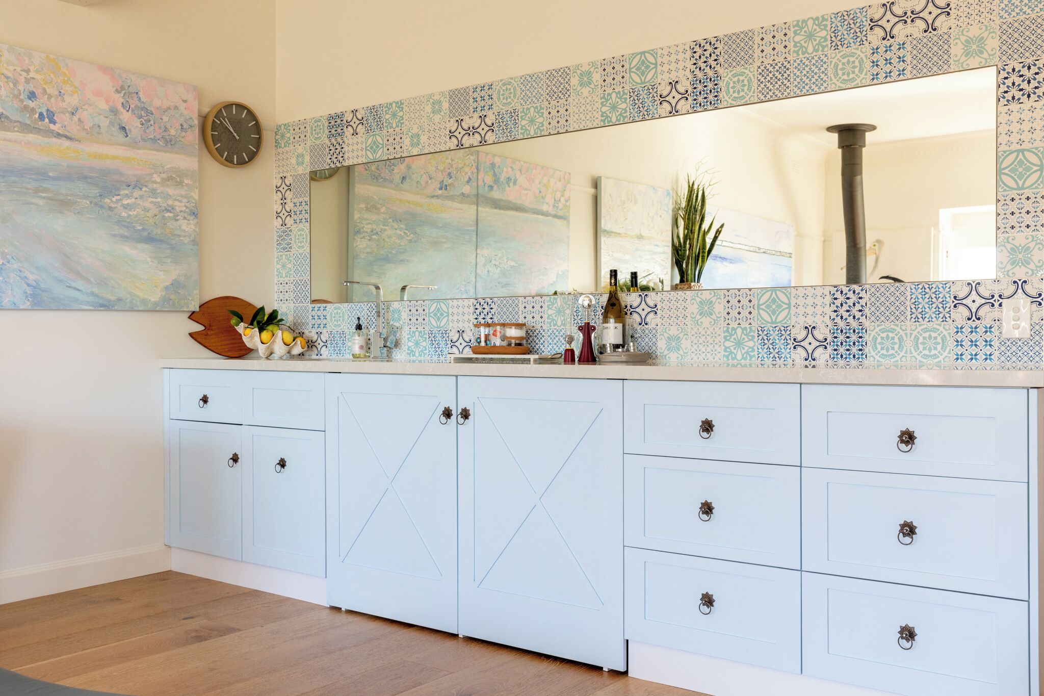A kitchen with a tiled backsplash, a large mirror, and a wooden cabinet with drawers.