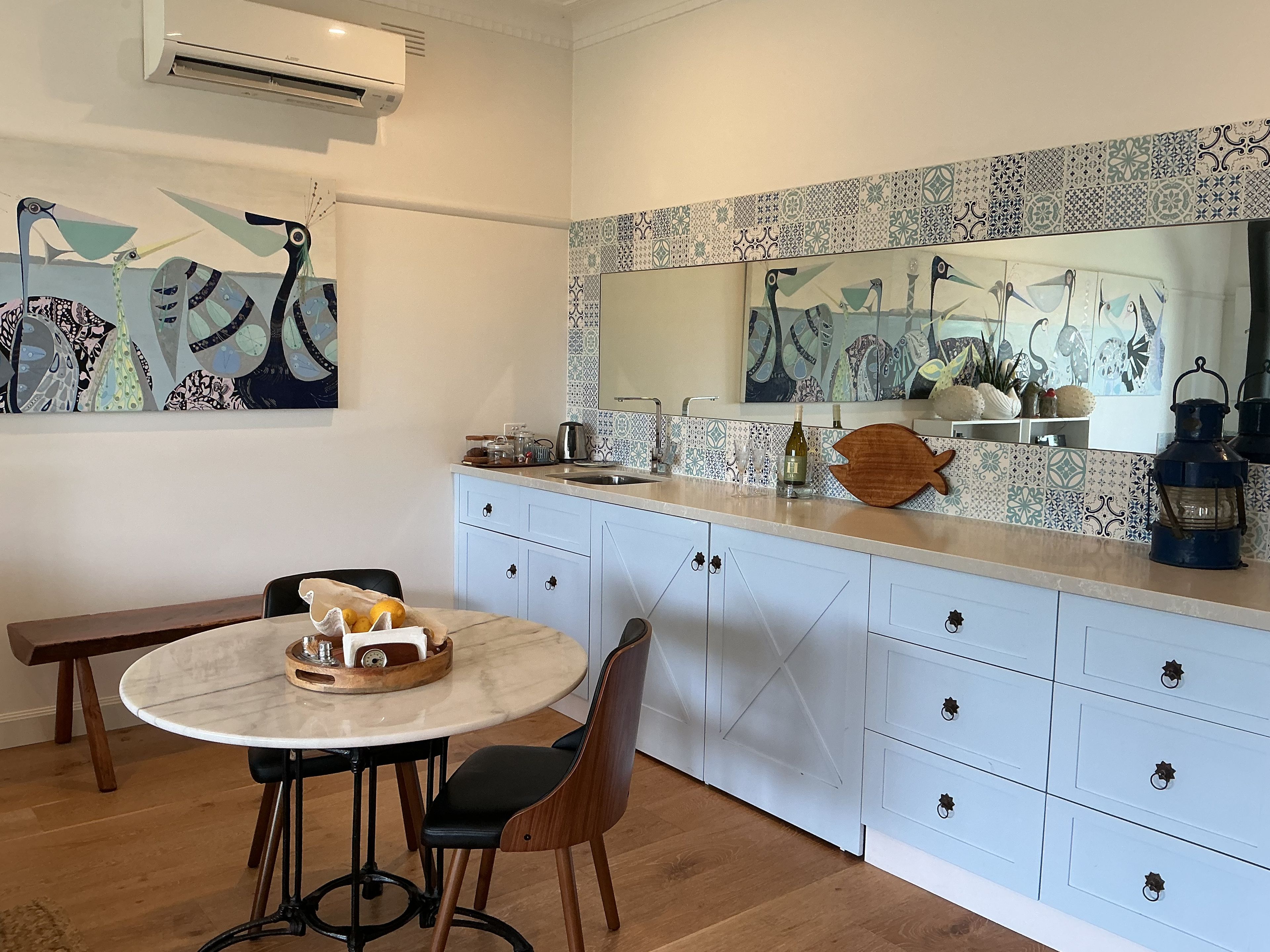 A modern kitchen with a round marble table, a wooden fish-shaped tray, and a large mirror above the counter.