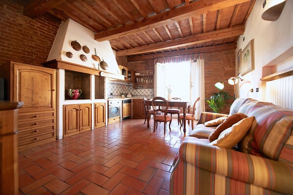 A rustic kitchen with wooden cabinets, a dining table, and a striped sofa. - Suite nell´ Anfiteatro Romano (Lucca)