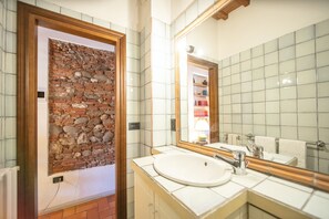 A bathroom with a stone wall, a sink, and a mirror. - Suite nell´ Anfiteatro Romano (Lucca)