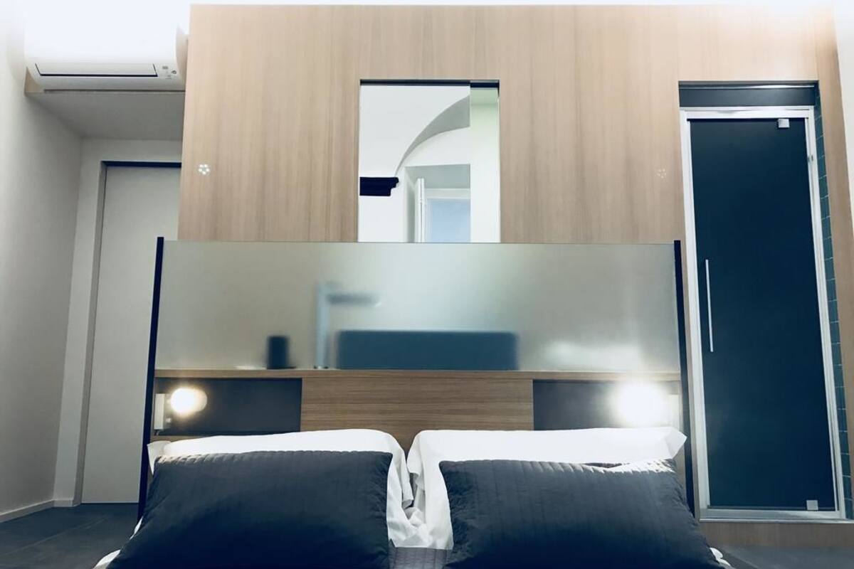 A hotel room with a bed, a wooden headboard, a mirror, and a door.