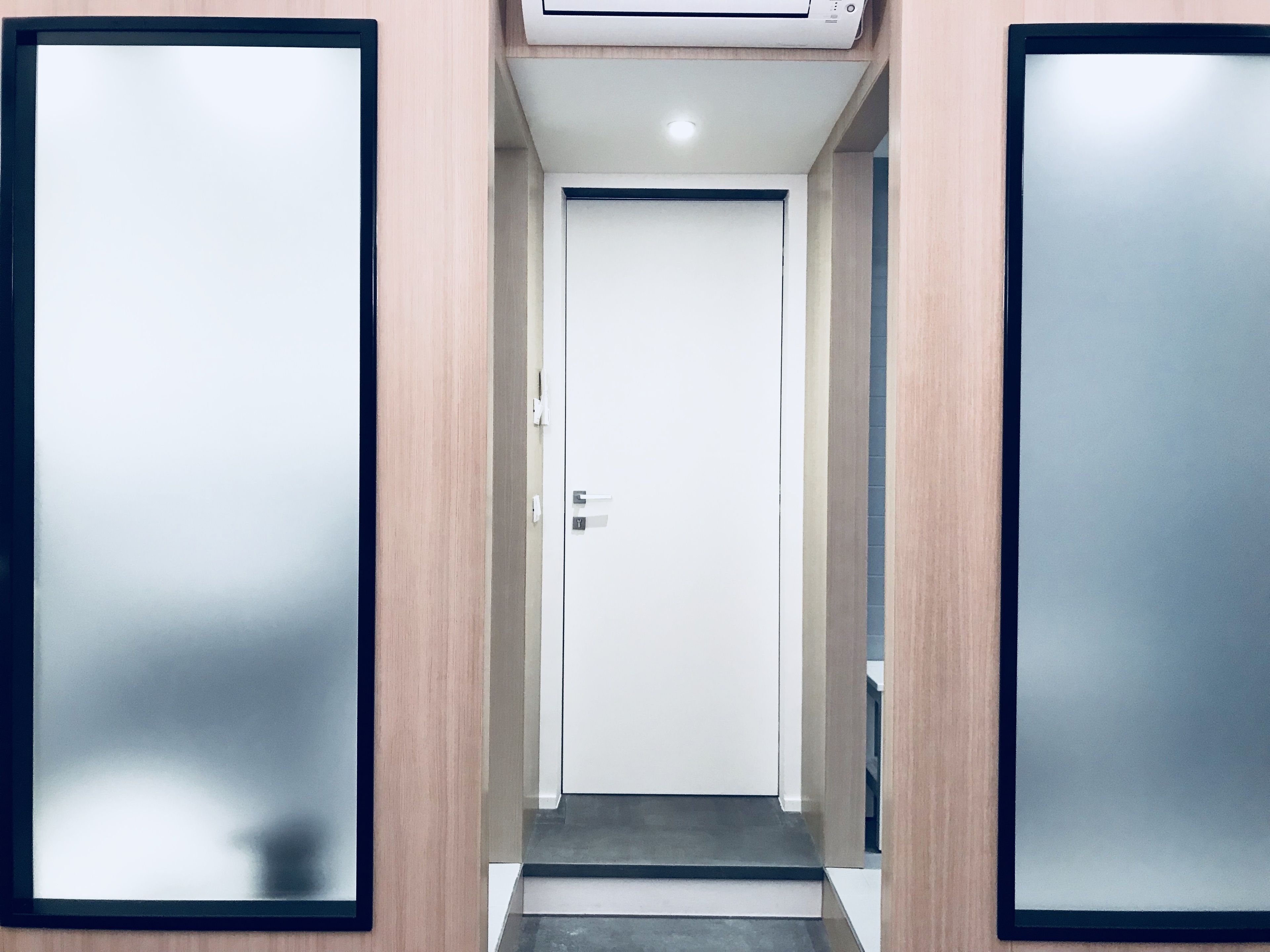 A hallway with a closed door at the end, flanked by two mirrored panels on the walls.